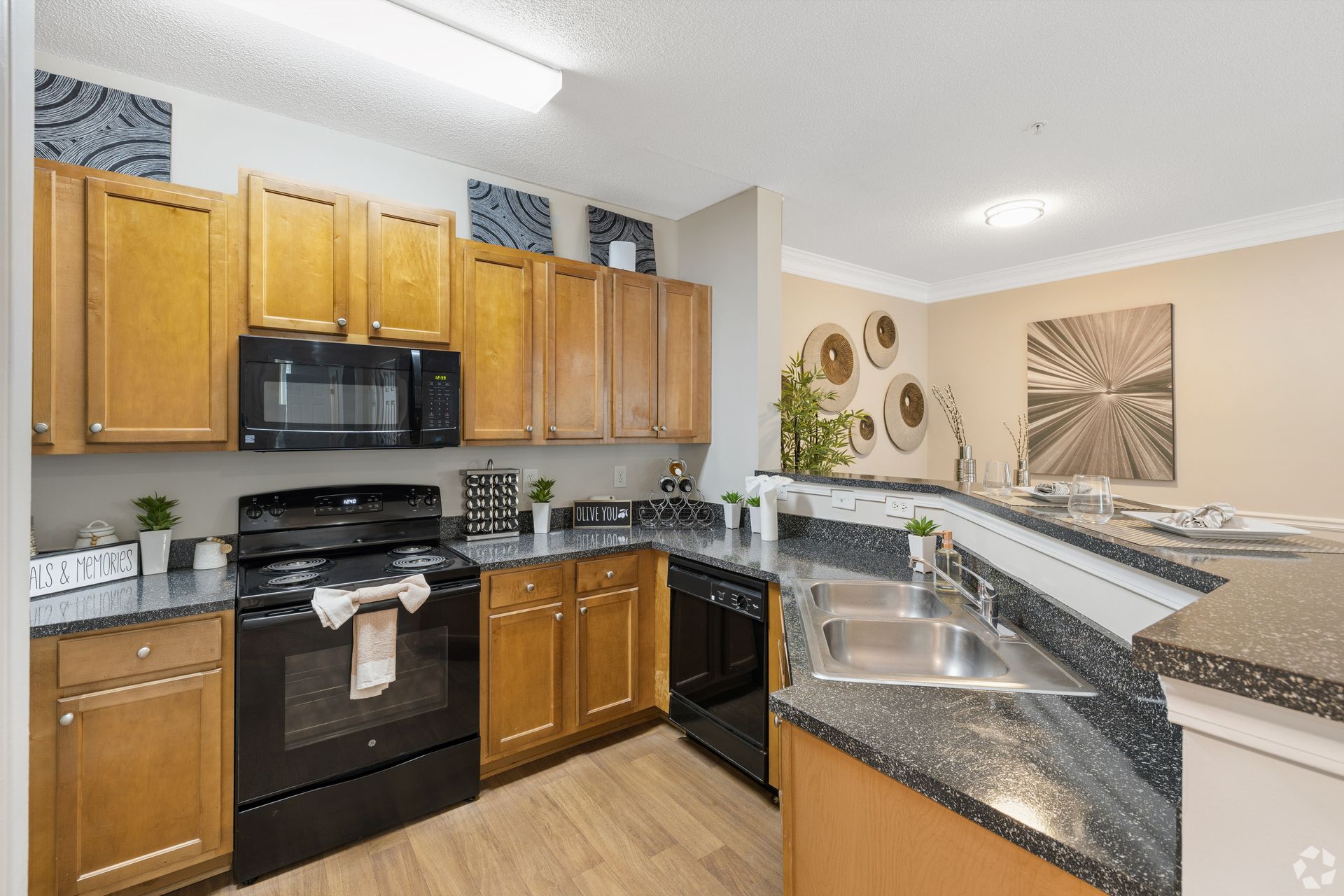 Bright kitchen with wood cabinets, black appliances, and speckled granite countertops
