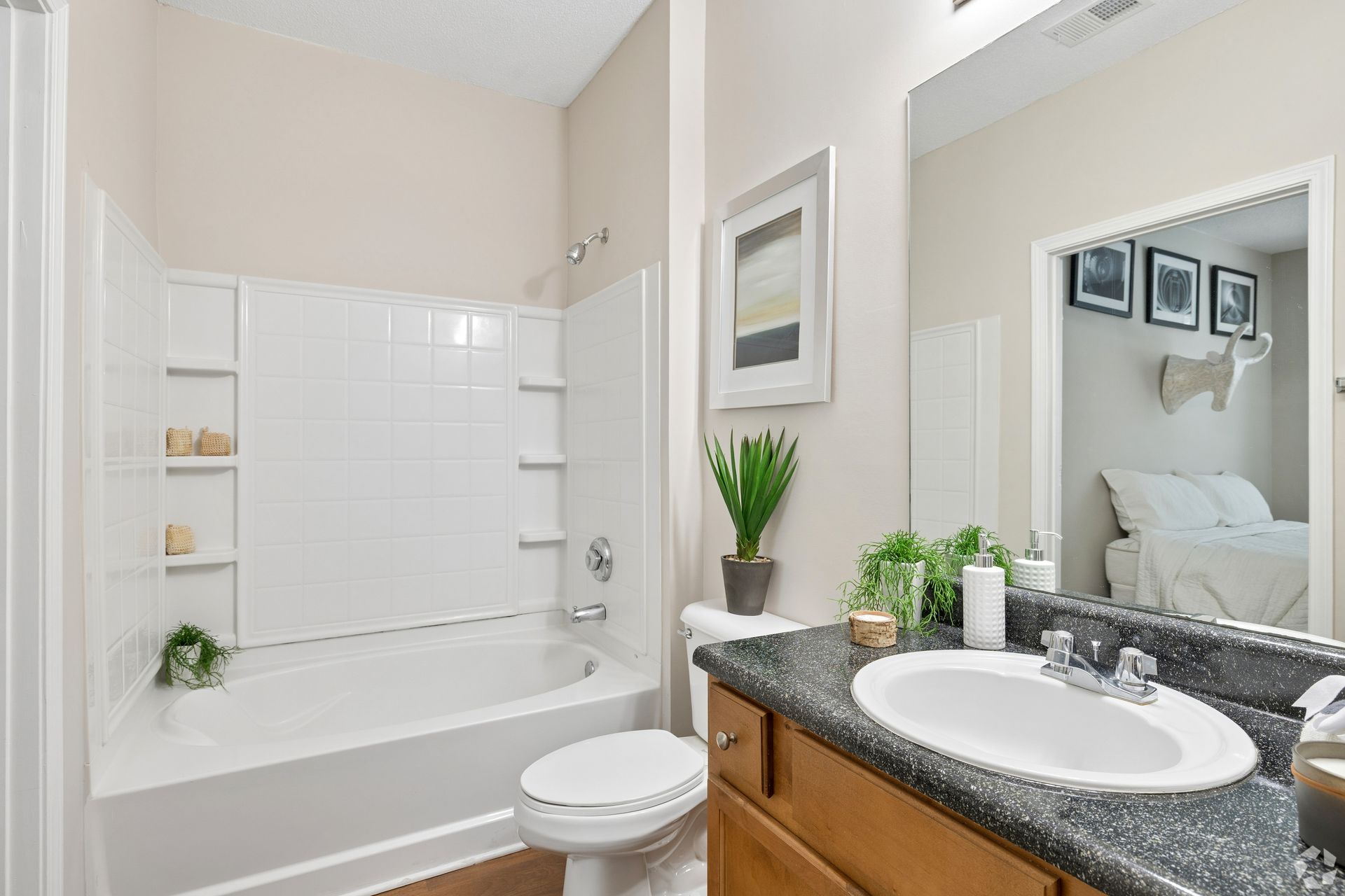 Bright bathroom with white tub, toilet, vanity, granite countertop, and mirror.