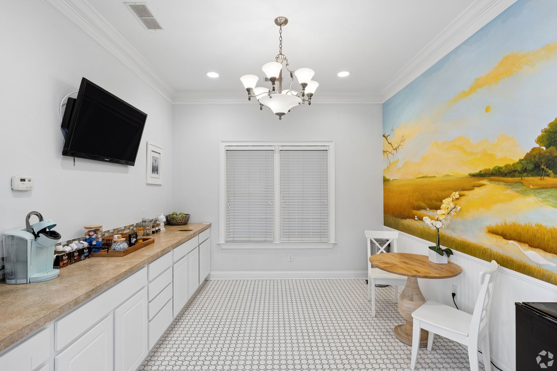 Bright dining nook with mural, white table, wall-mounted TV, and sideboard cabinets under a chandelier.
