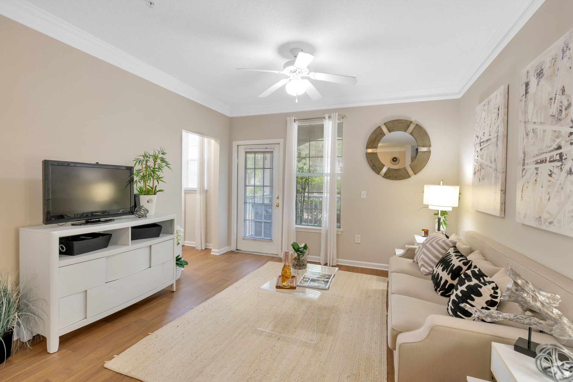 Bright beige living room with sofa, TV console, wall mirror, and large windows.