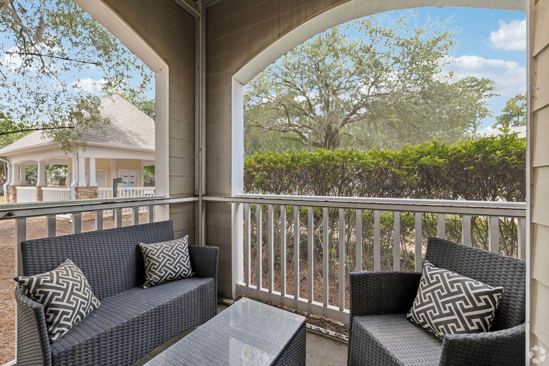 Covered balcony with wicker chairs and patterned pillows overlooking trees and neighboring homes