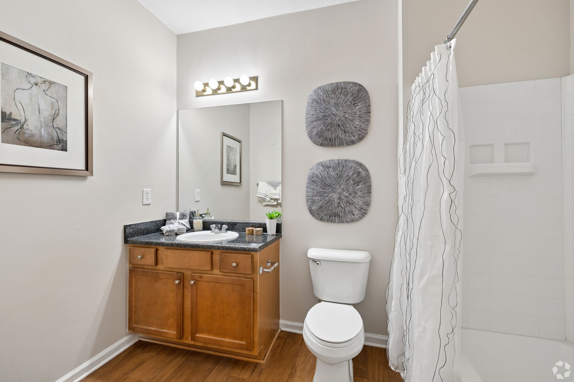 Small bathroom with wooden vanity, toilet, mirror, and white shower curtain.