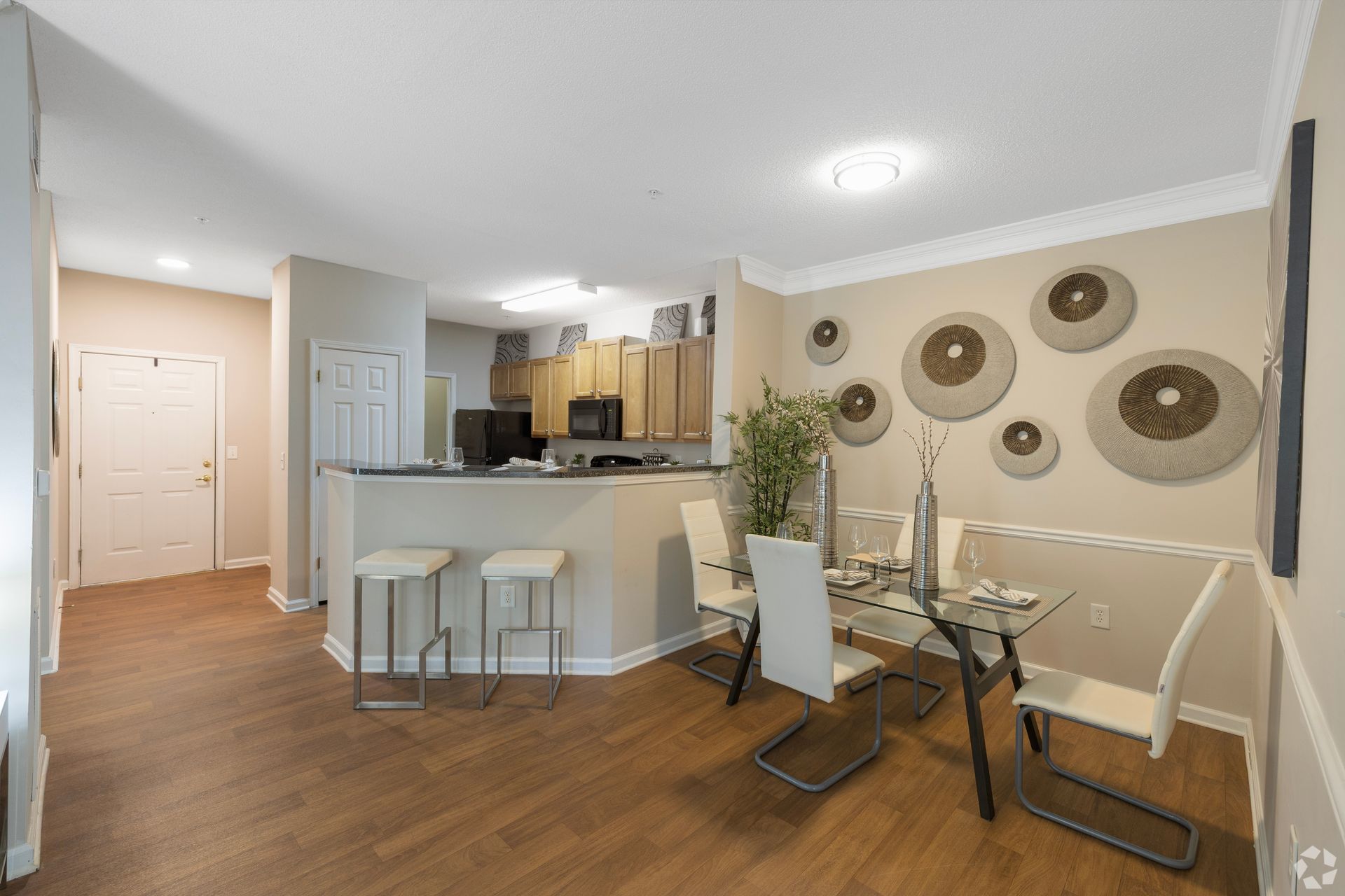 Open-concept dining and kitchen with glass table, white bar stools, wood floors, and wall decor