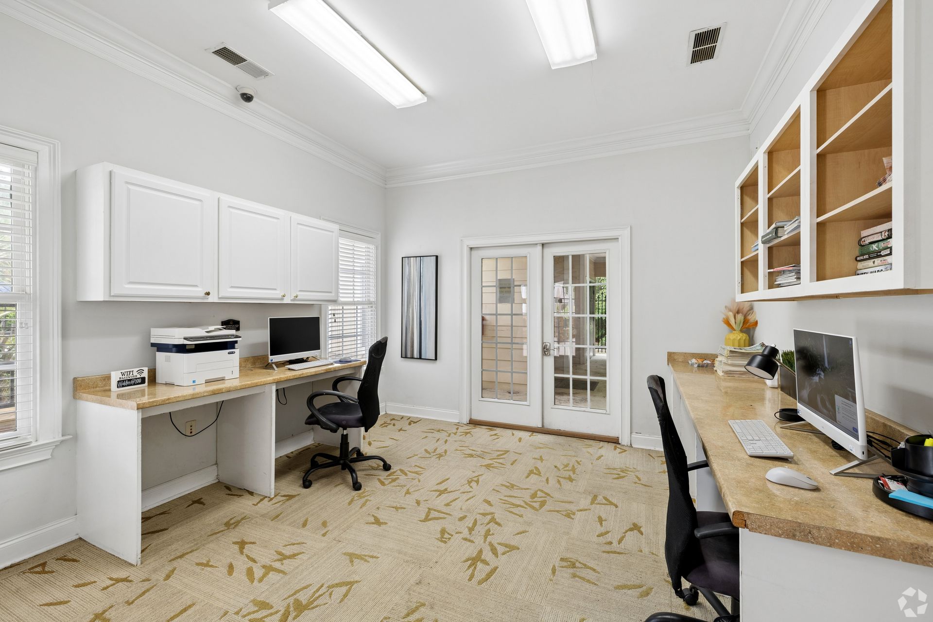 Bright home office with white cabinets, two desks, black chairs, and French doors in back.