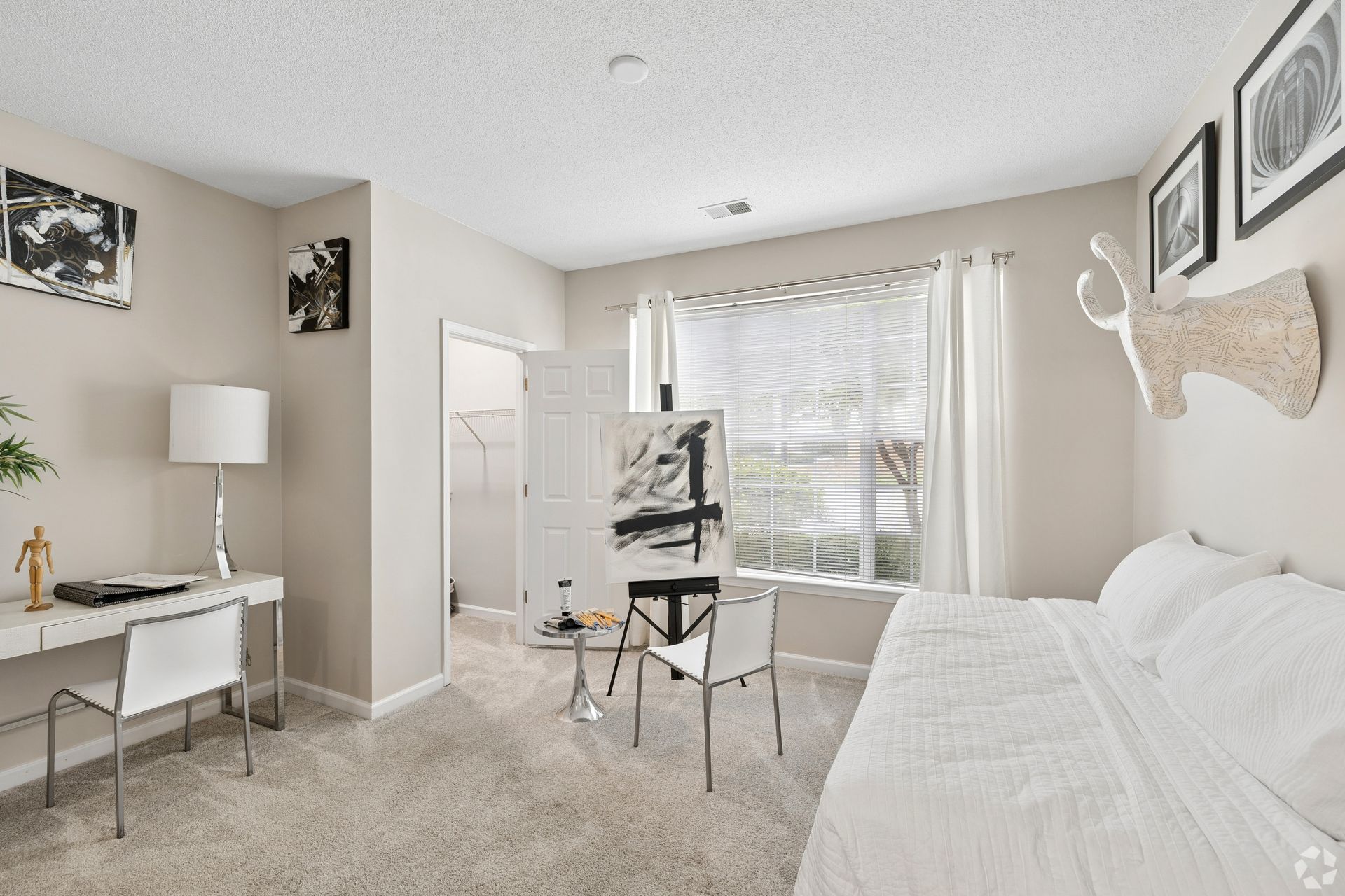 Bright beige bedroom-office with desk, chair, window blinds, and white bed.