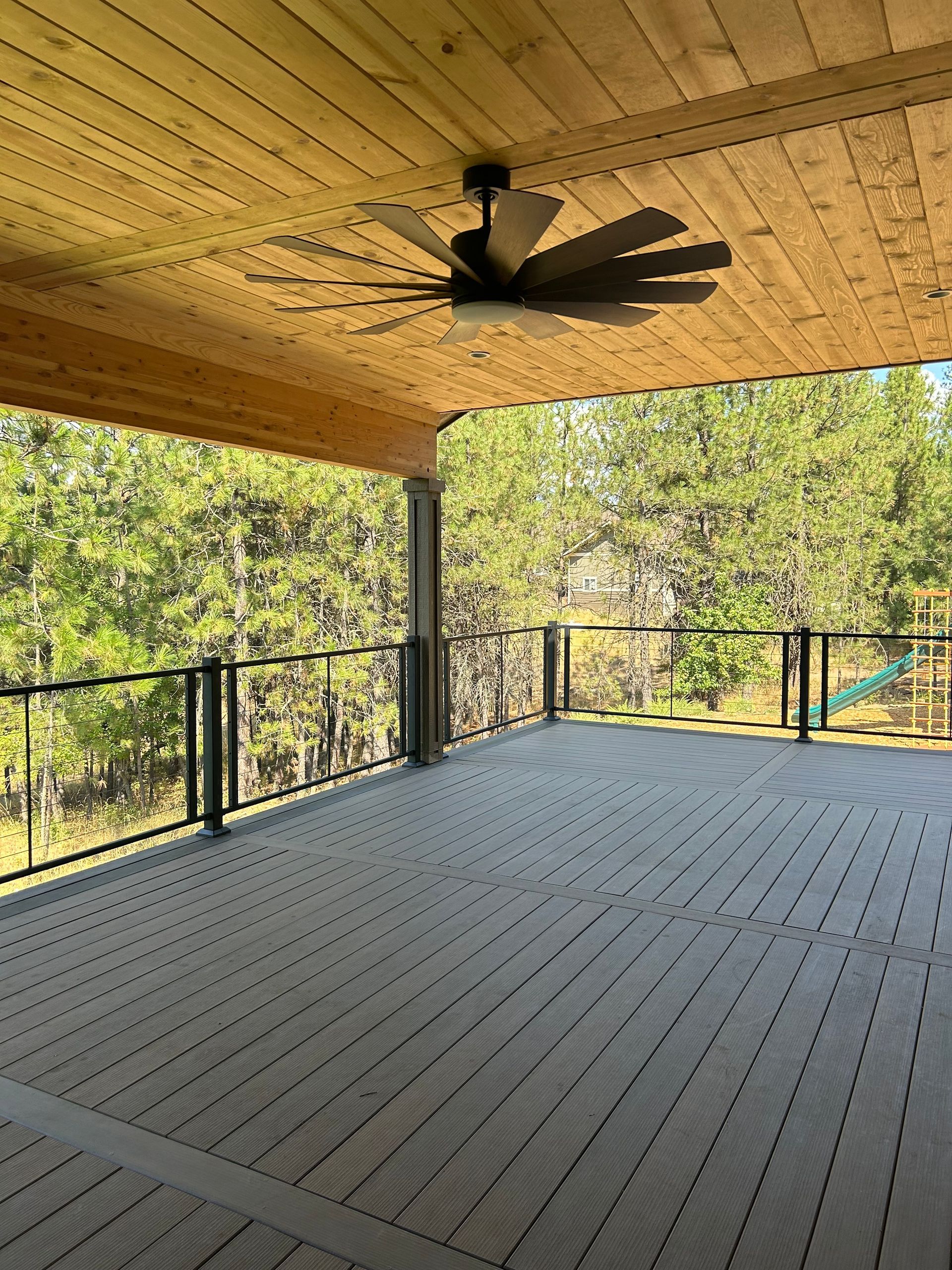 An empty deck with a ceiling fan and trees in the background.