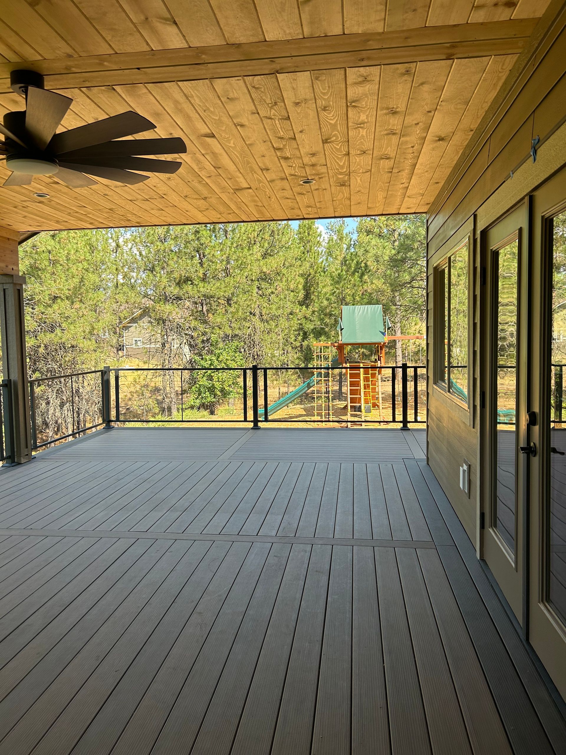 A large deck with a ceiling fan and a playground in the background.
