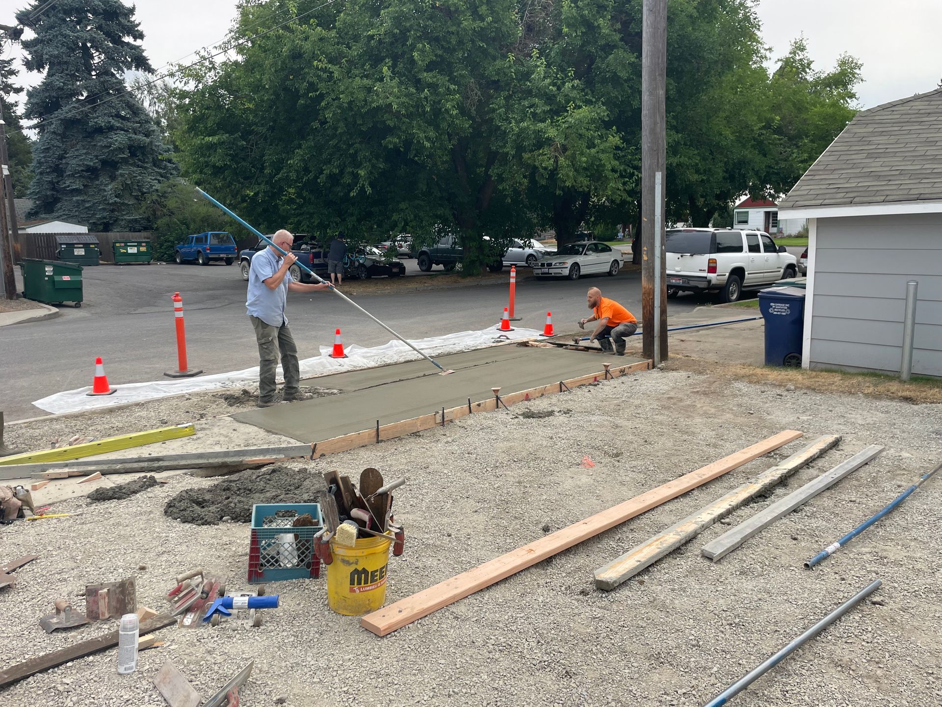 Two men are working on a sidewalk in a gravel area.