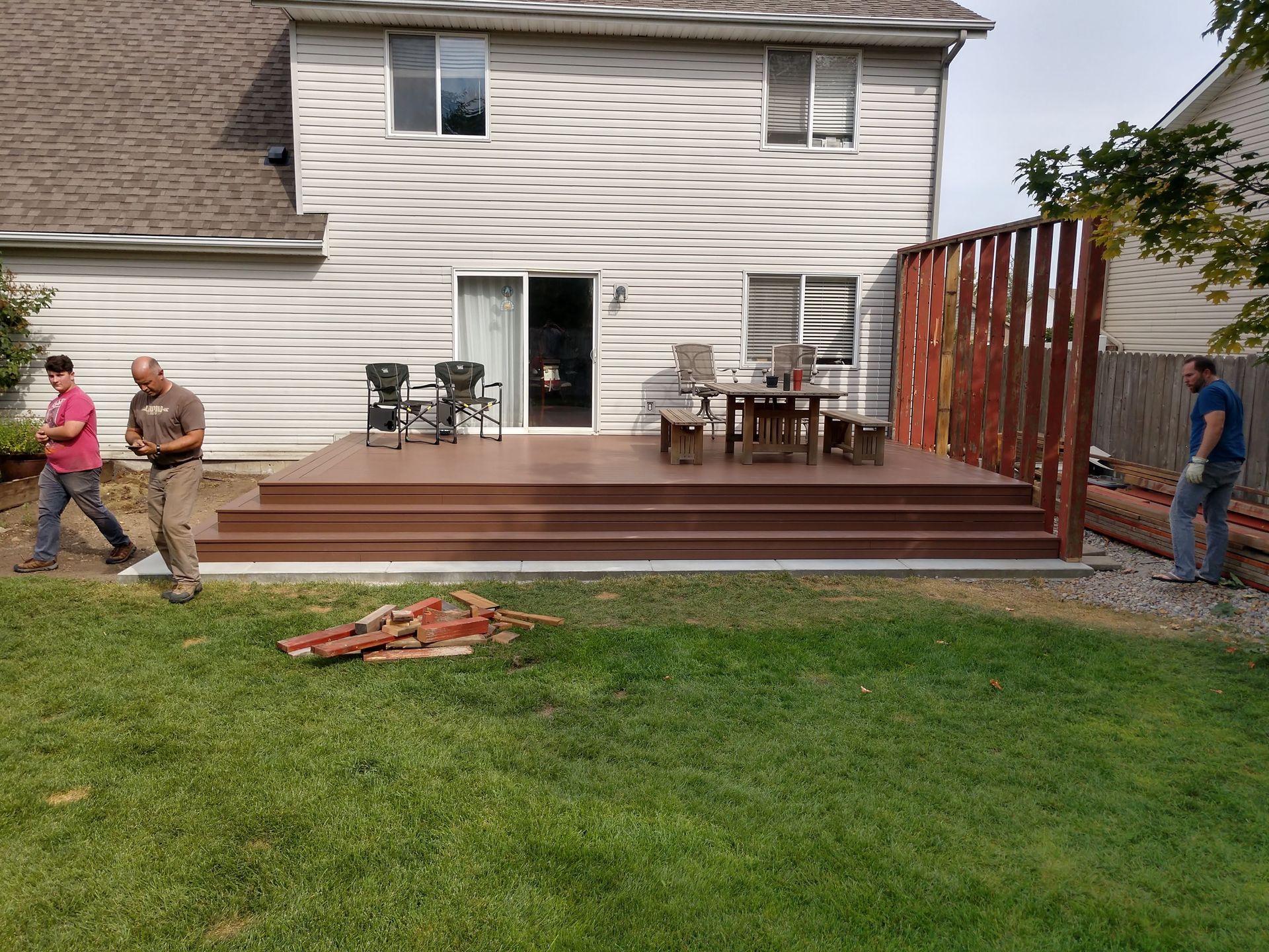 Two men are working on a deck in the backyard of a house.