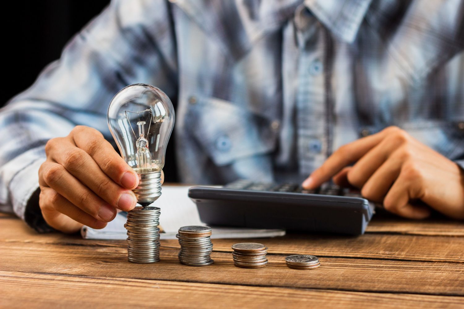 Incentivos tributarios energías renovables en Colombia Una persona está colocando una bombilla encima de una pila de monedas.