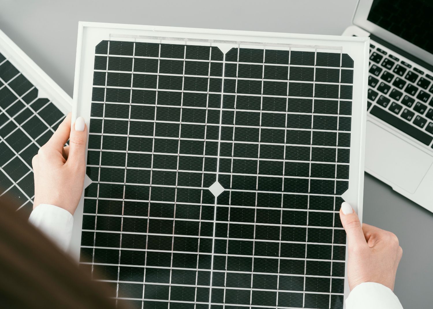 Una persona sostiene un panel solar frente a una computadora portátil.