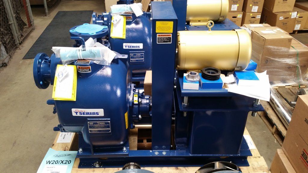 A blue industrial pump unit with a yellow motor mounted on a wooden pallet inside a warehouse.