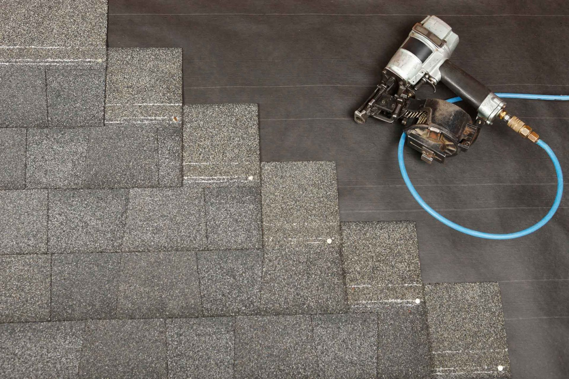 Roof shingles with a worker’s hand tool and blue hose at the upper right edge Roof shingles with a worker’s hand tool and blue hose at the upper right edge