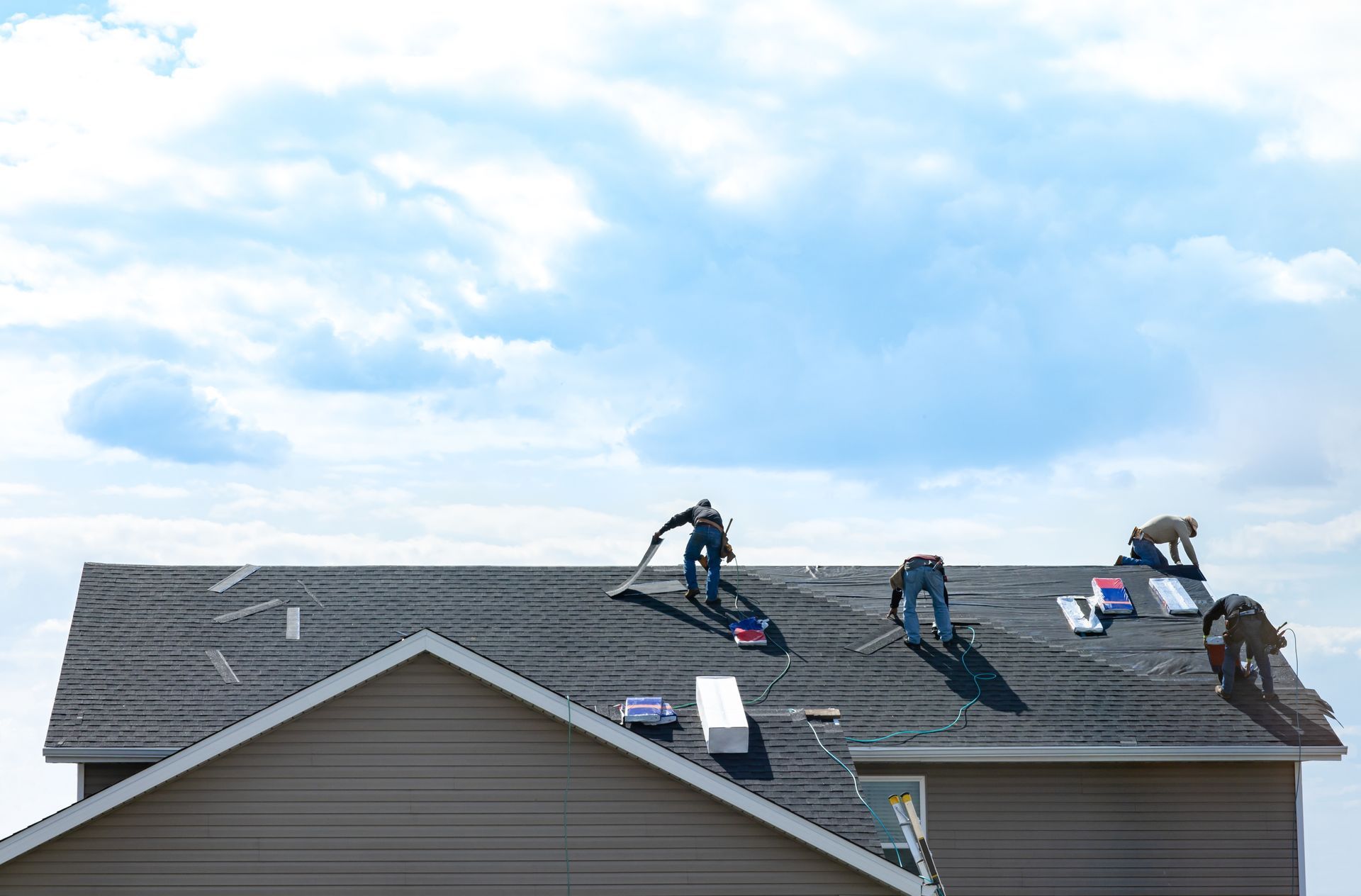 A roofing crew installing new shingles on a house rooftop while working with tools