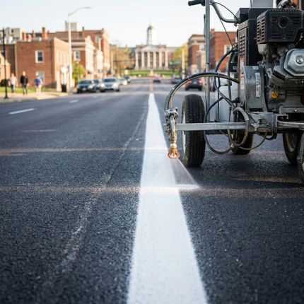 Worker using line striping machine to apply white line on asphalt parking lot for traffic control
