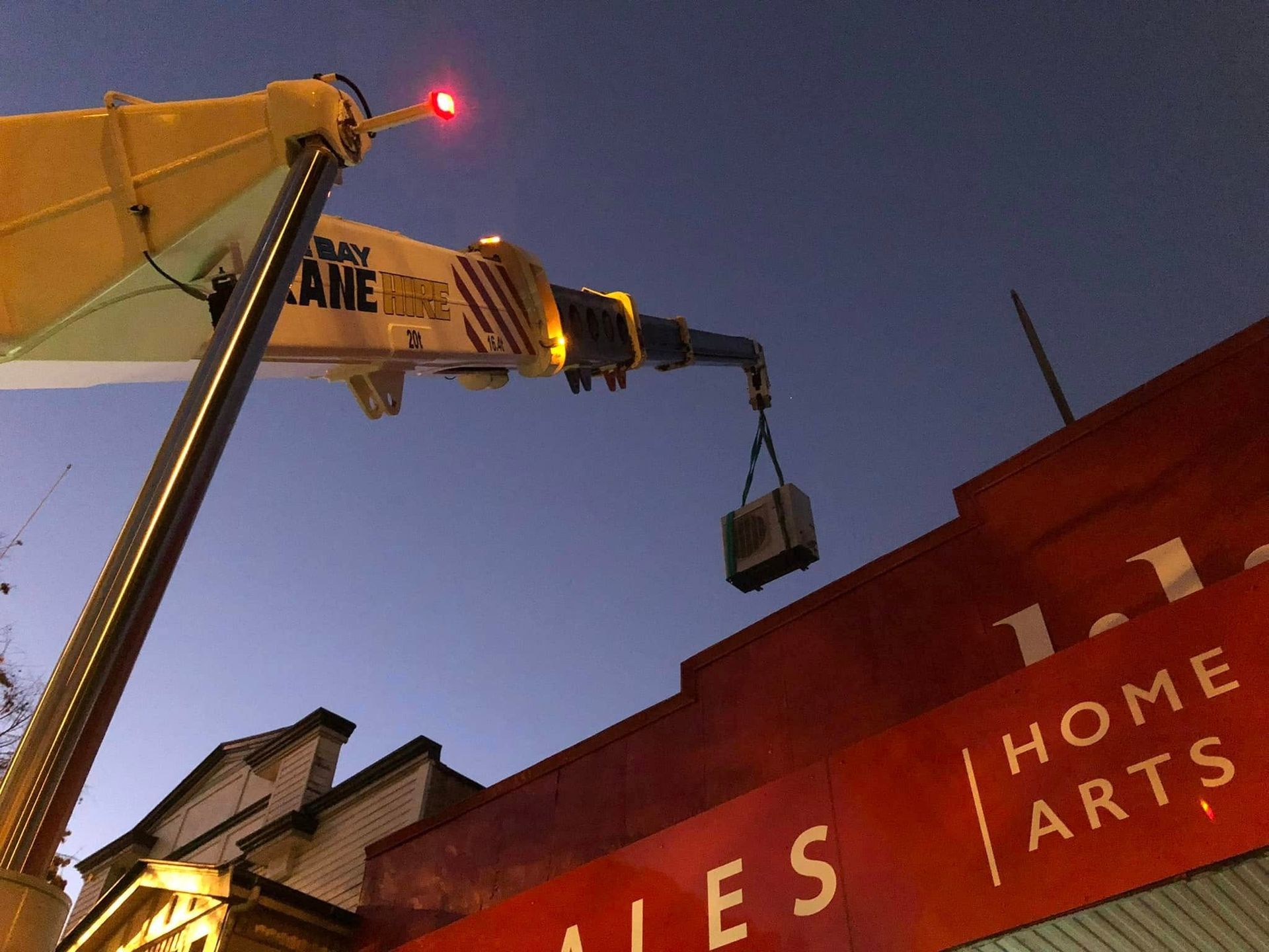 Crane Hoisting a Load Beside a Red Building at Dusk — A & T Air-Conditioning and Refrigeration in Millbank, QLD