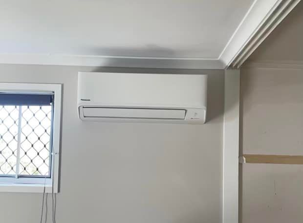 Wall-mounted White Air Conditioner Above a Window in a Gray Room — A & T Air-Conditioning and Refrigeration in Millbank, QLD