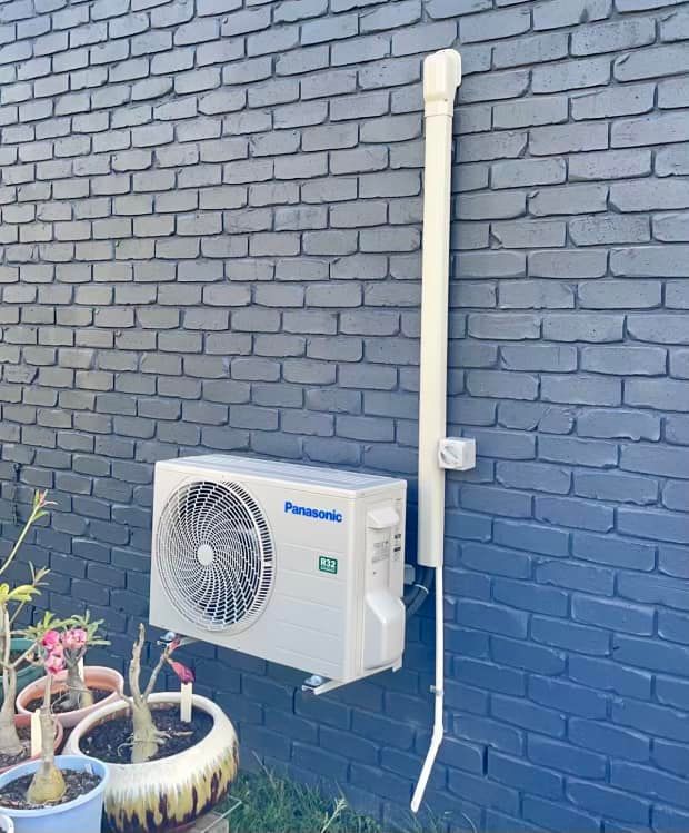 Outdoor Air Conditioner Unit Mounted on a Dark Brick Wall — A & T Air-Conditioning and Refrigeration in Millbank, QLD