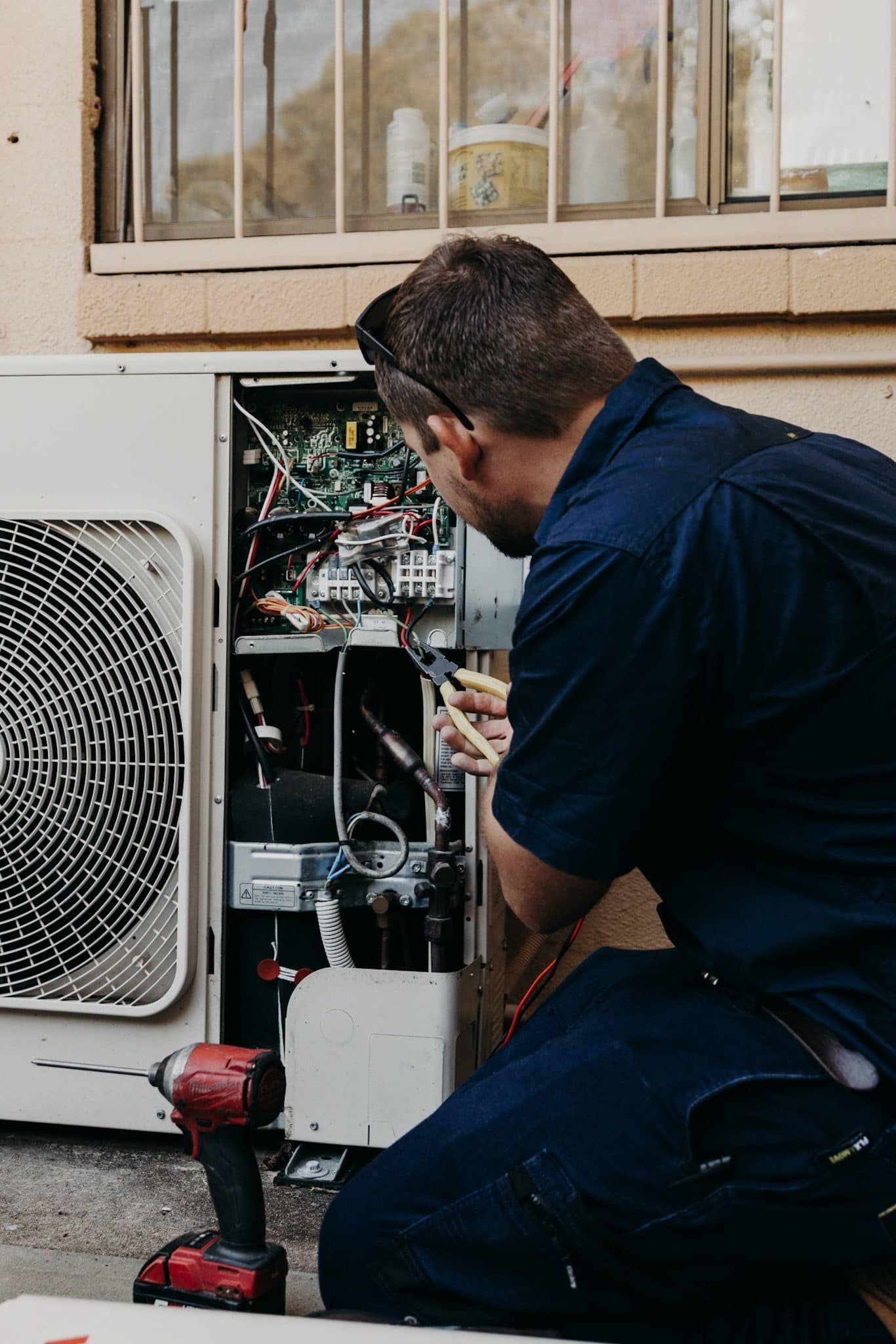 Technician Kneeling Beside Outdoor HVAC Unit — A & T Air-Conditioning and Refrigeration in Millbank, QLD