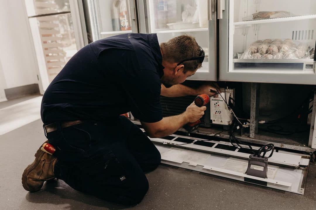 Technician Kneeling and Repairing an Open Refrigerator — A & T Air-Conditioning and Refrigeration in Millbank, QLD