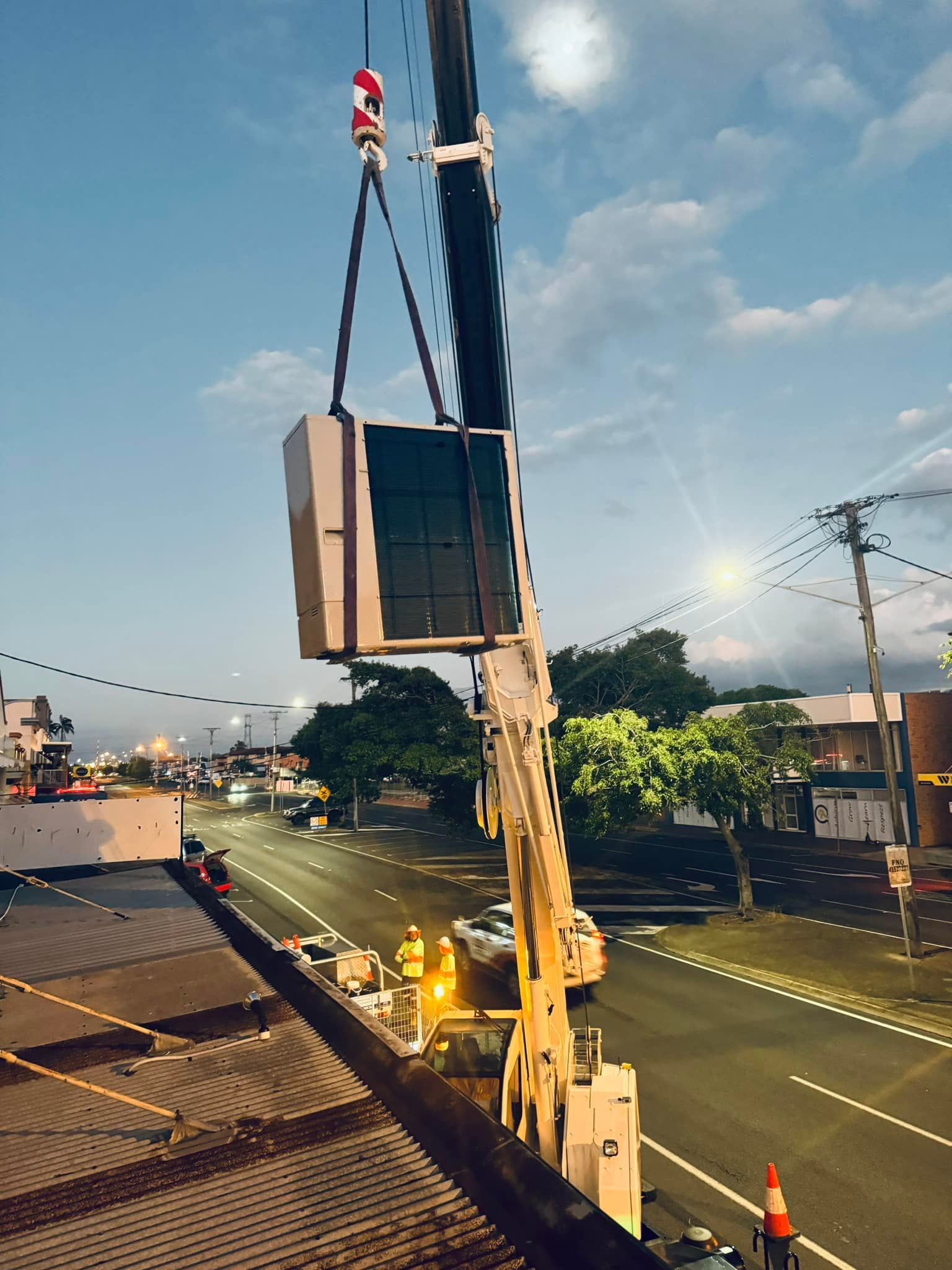 Crane Lifting a Large Box Over a Roadside at Dusk — A & T Air-Conditioning and Refrigeration in Millbank, QLD