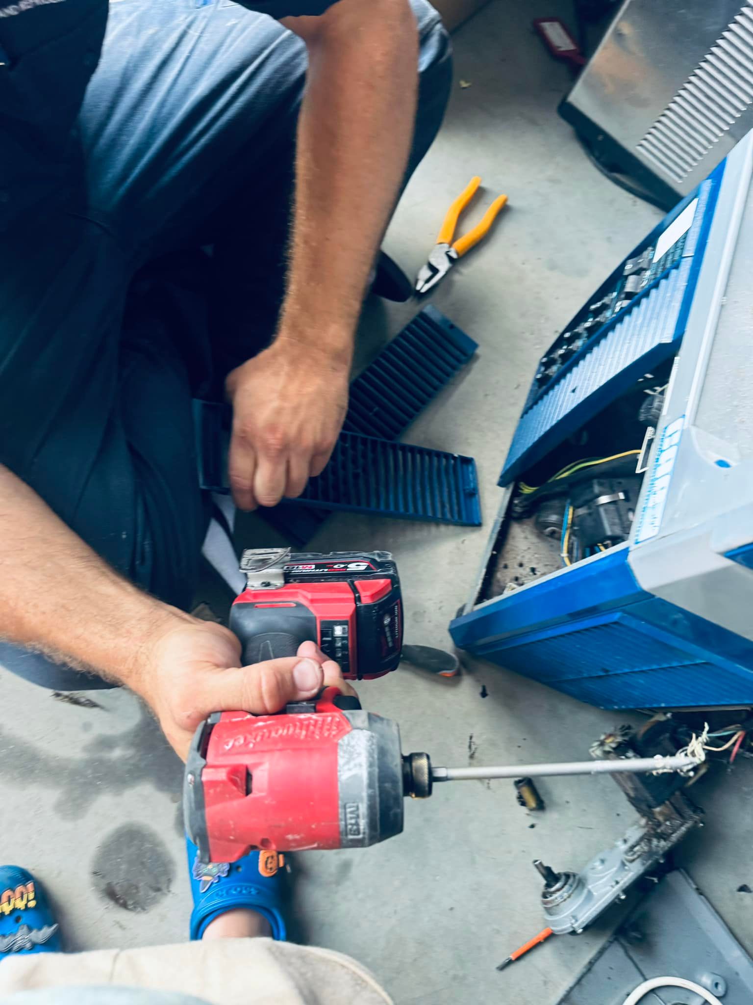 Person Using a Power Tool to Work on a Blue Machine in a Workshop — A & T Air-Conditioning and Refrigeration in Millbank, QLD