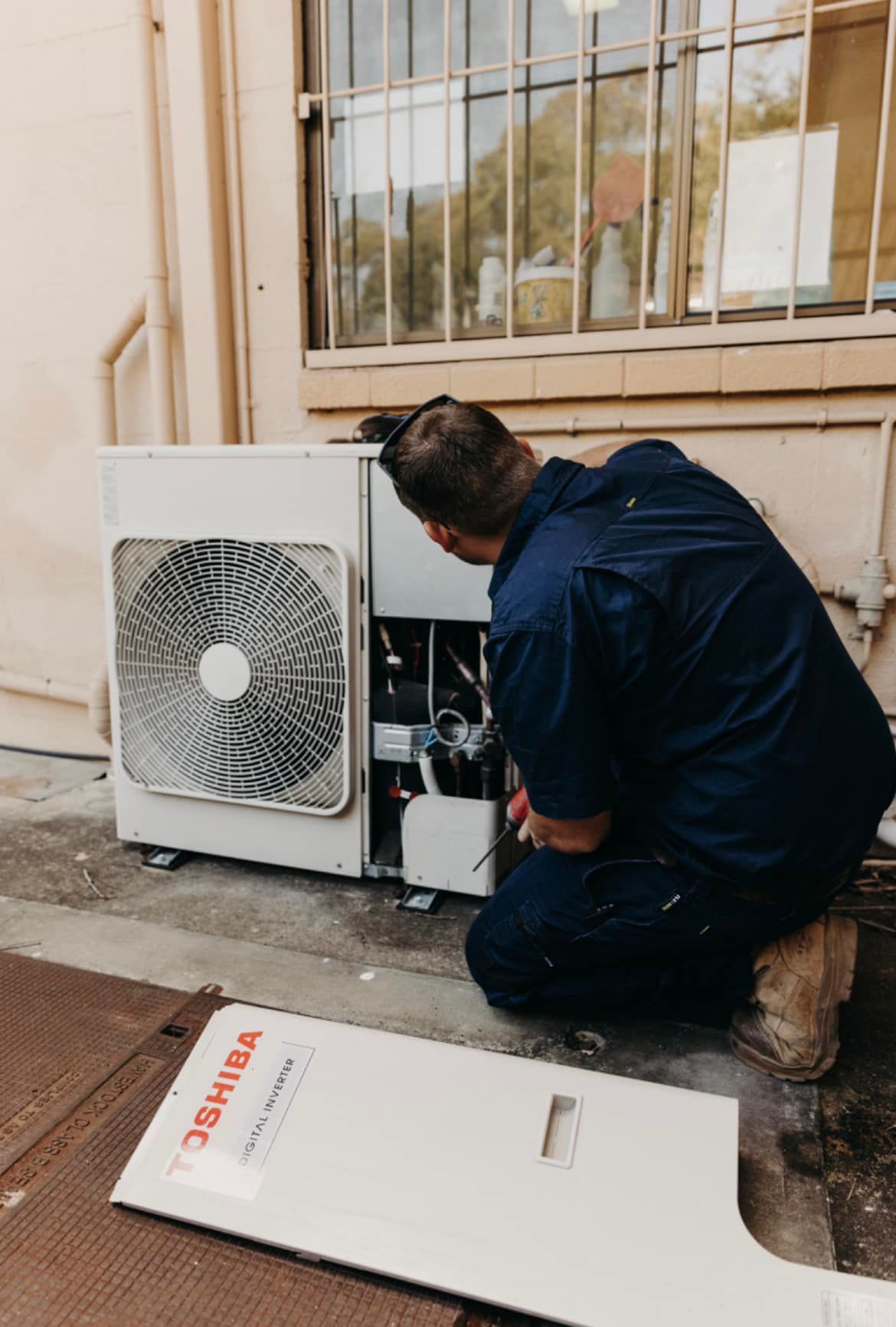 Technician Kneeling Beside an Outdoor Air Conditioner Unit — A & T Air-Conditioning and Refrigeration in Millbank, QLD