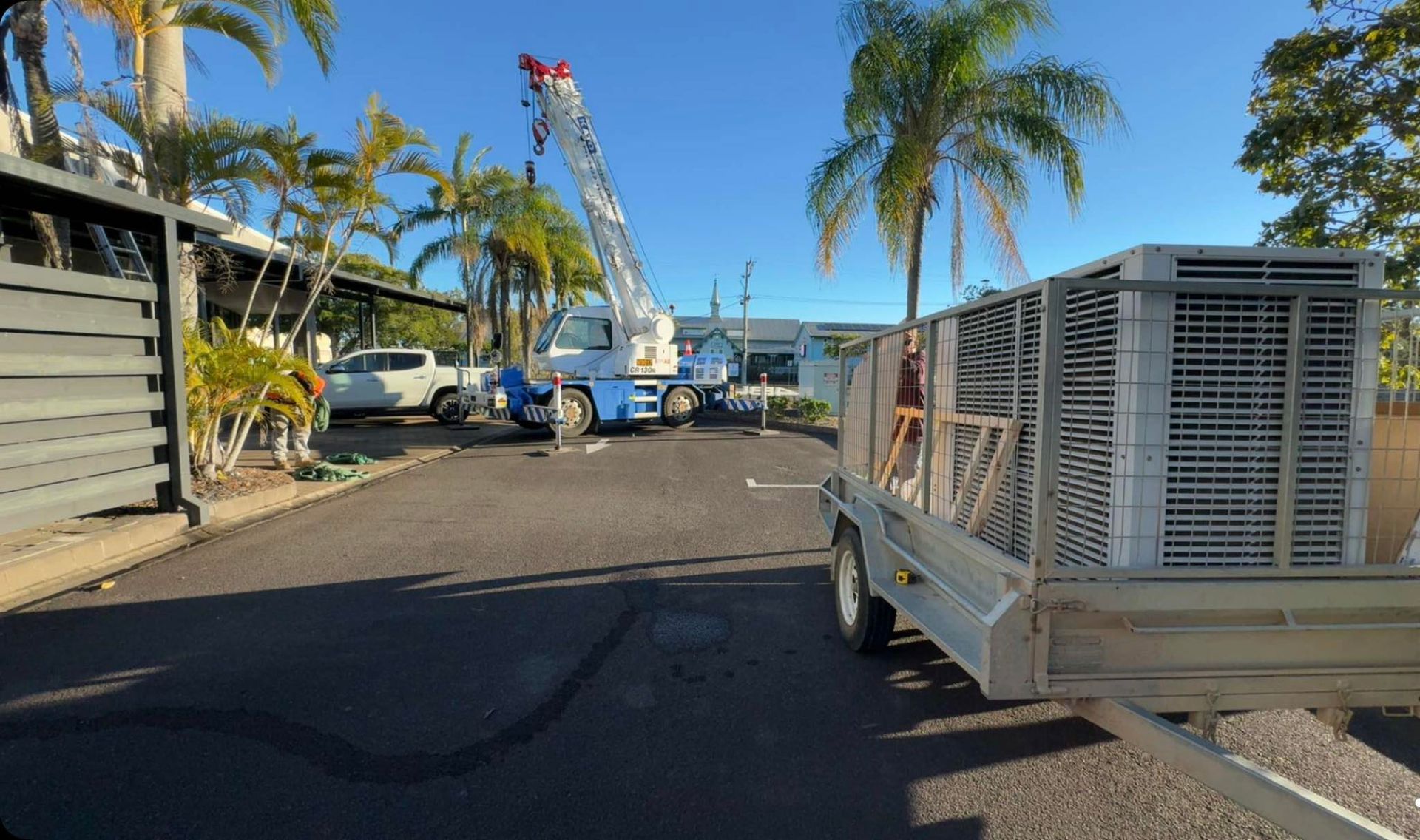 Construction Crane and Trailer on a Street Lined With Palm Trees — A & T Air-Conditioning and Refrigeration in Millbank, QLD