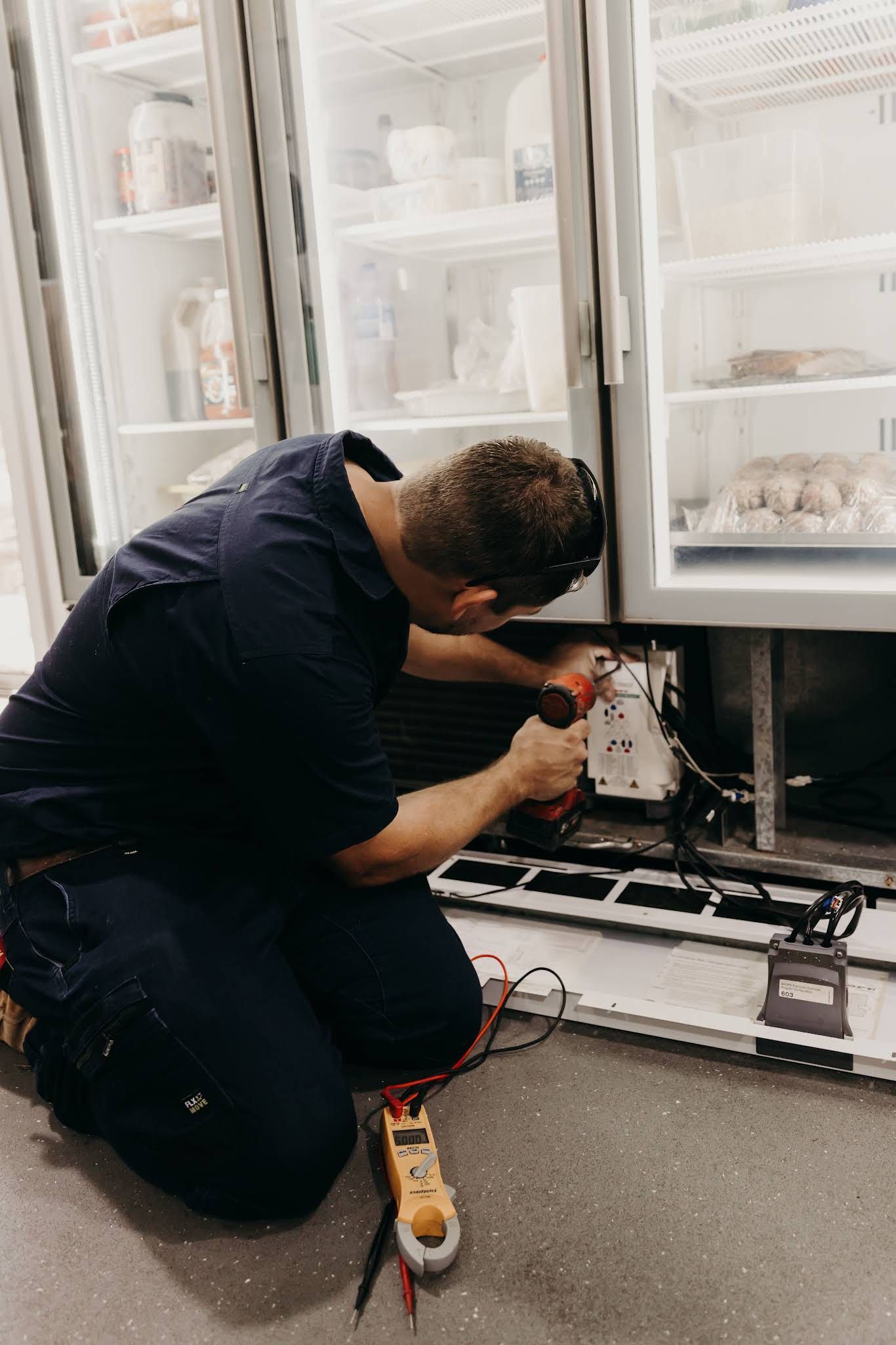 Technician Kneels Repairing Wiring at an Open Refrigerator — A & T Air-Conditioning and Refrigeration in Millbank, QLD