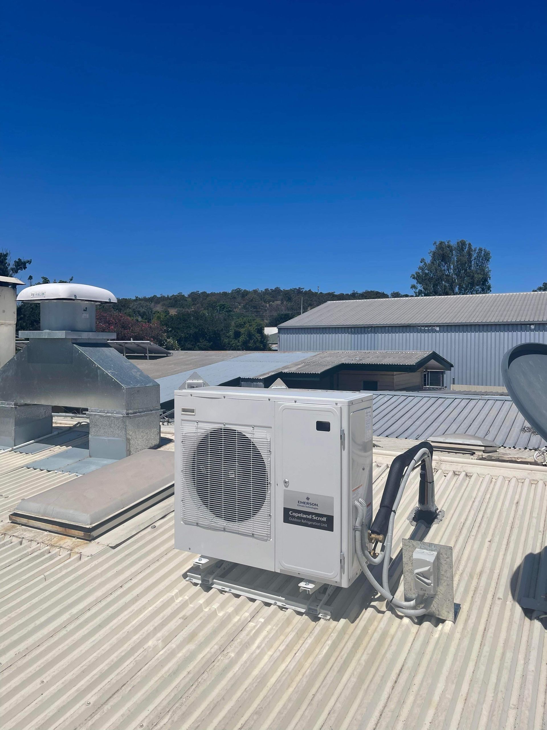 White HVAC Unit on a Corrugated Rooftop Under a Clear Blue Sky — A & T Air-Conditioning and Refrigeration in Millbank, QLD