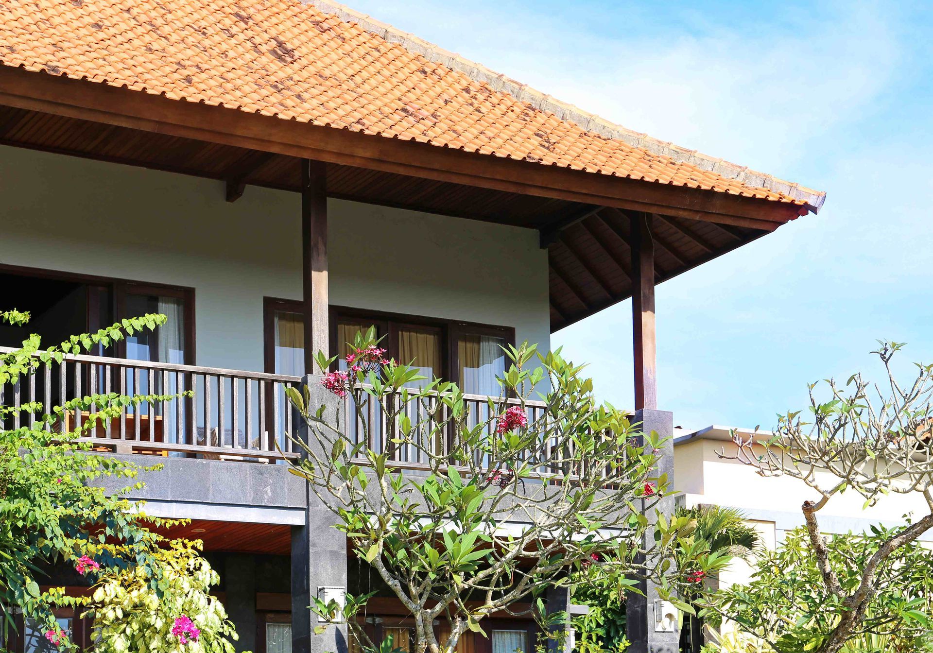 Traditional house with a tiled roof, wooden balcony, and lush greenery under a bright blue sky