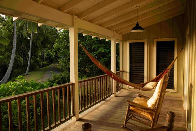 Wooden porch with a hammock and rocking chair overlooking lush green trees at sunset