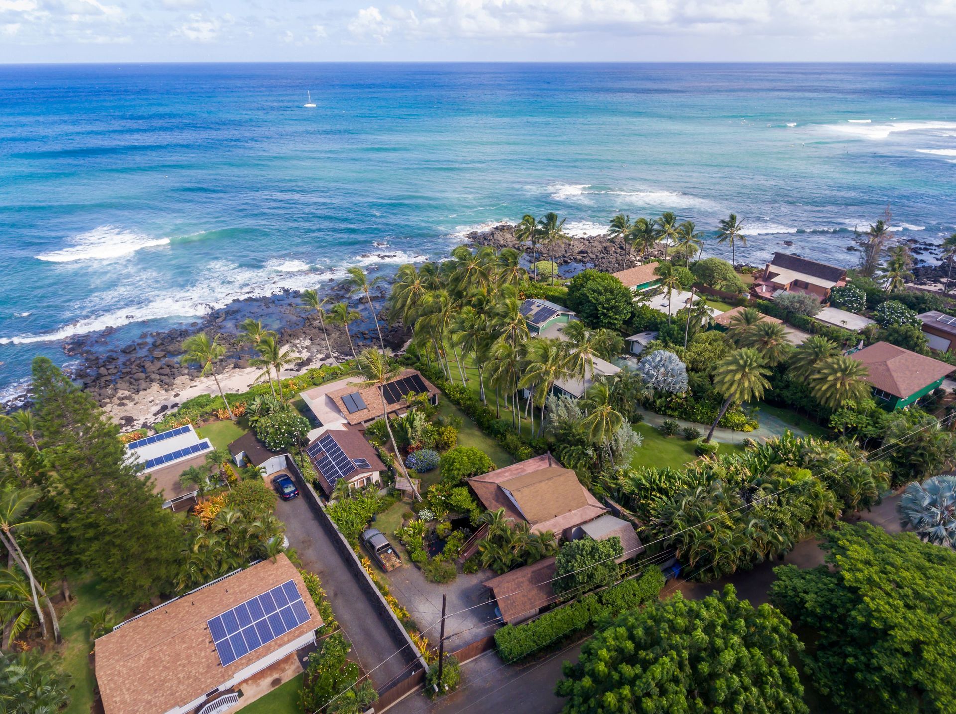 Aerial view of a tropical coastal resort with palm trees, villas, and ocean waves