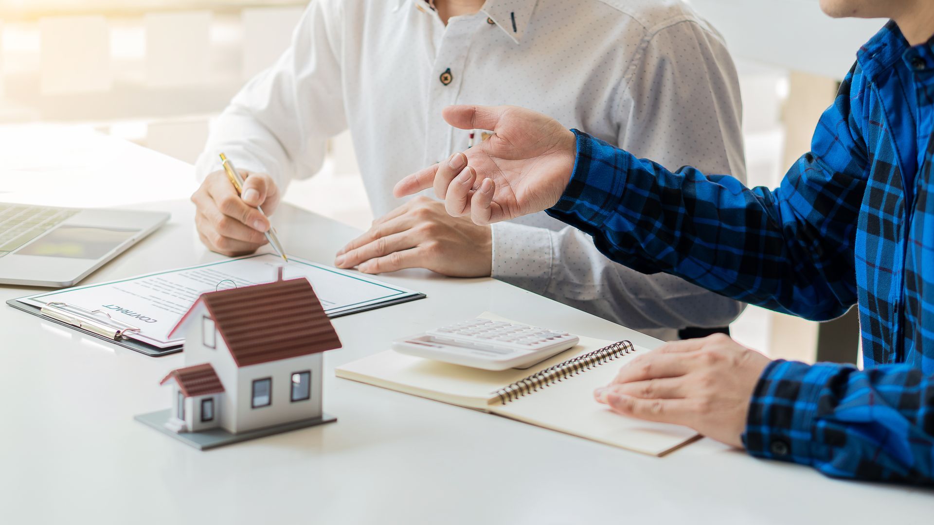 Two people discussing a house model and paperwork at a bright table