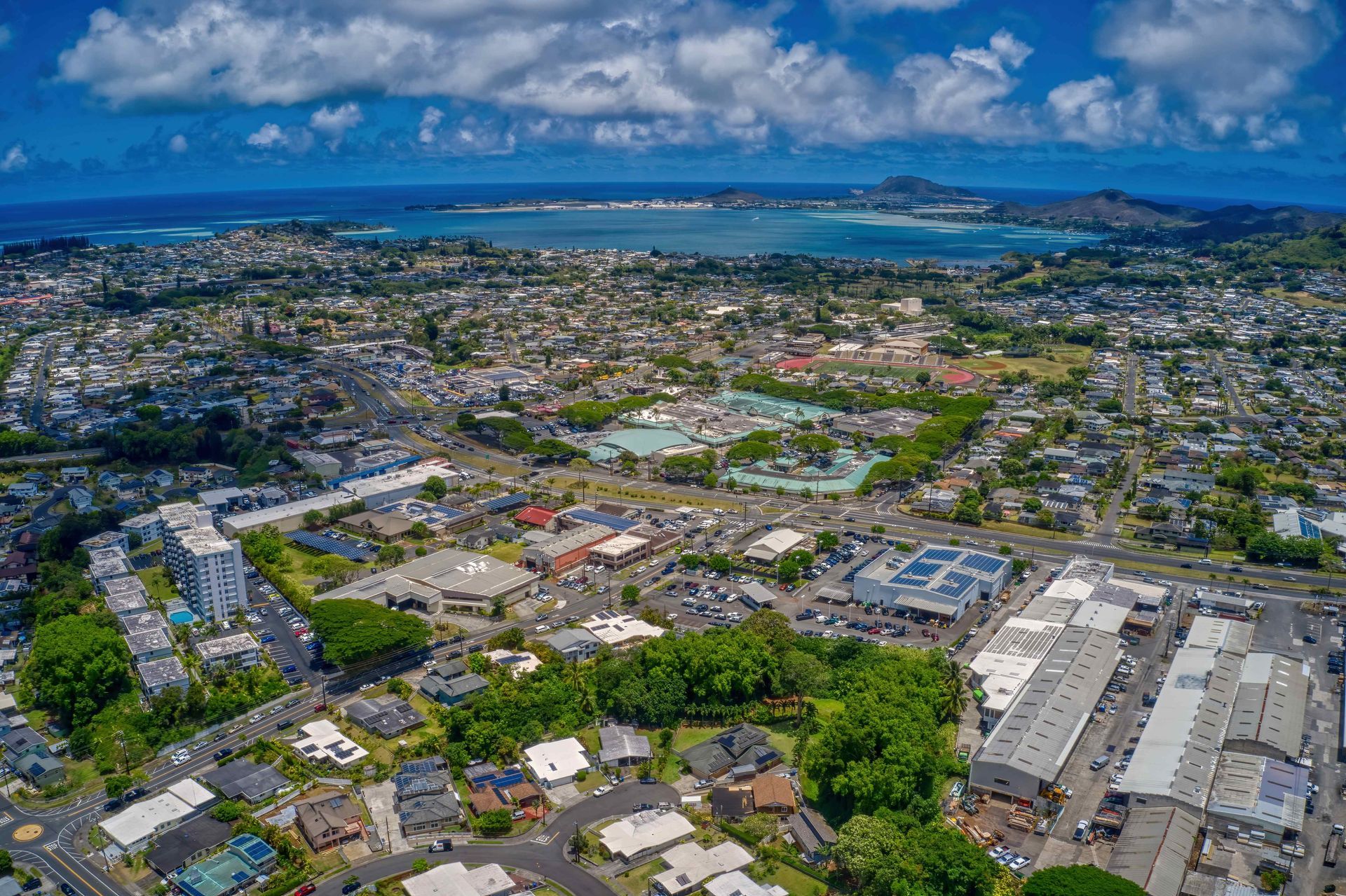 Aerial view of a coastal city with neighborhoods, roads, and blue ocean under a partly cloudy sky
