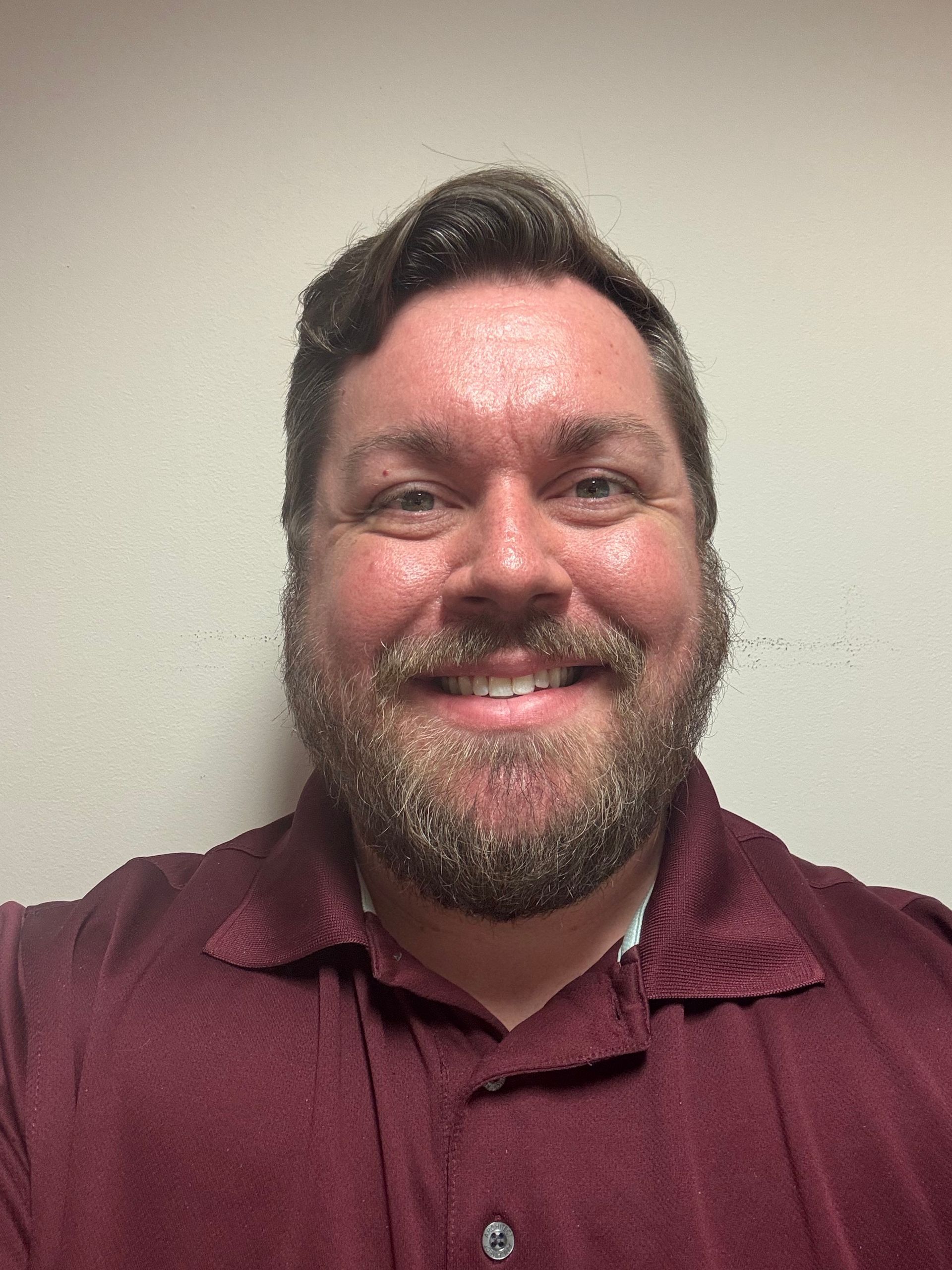 A man is smiling in front of a window in a room.