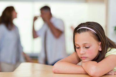 Child at a table A sad child sitting at a table while parents argue in the background