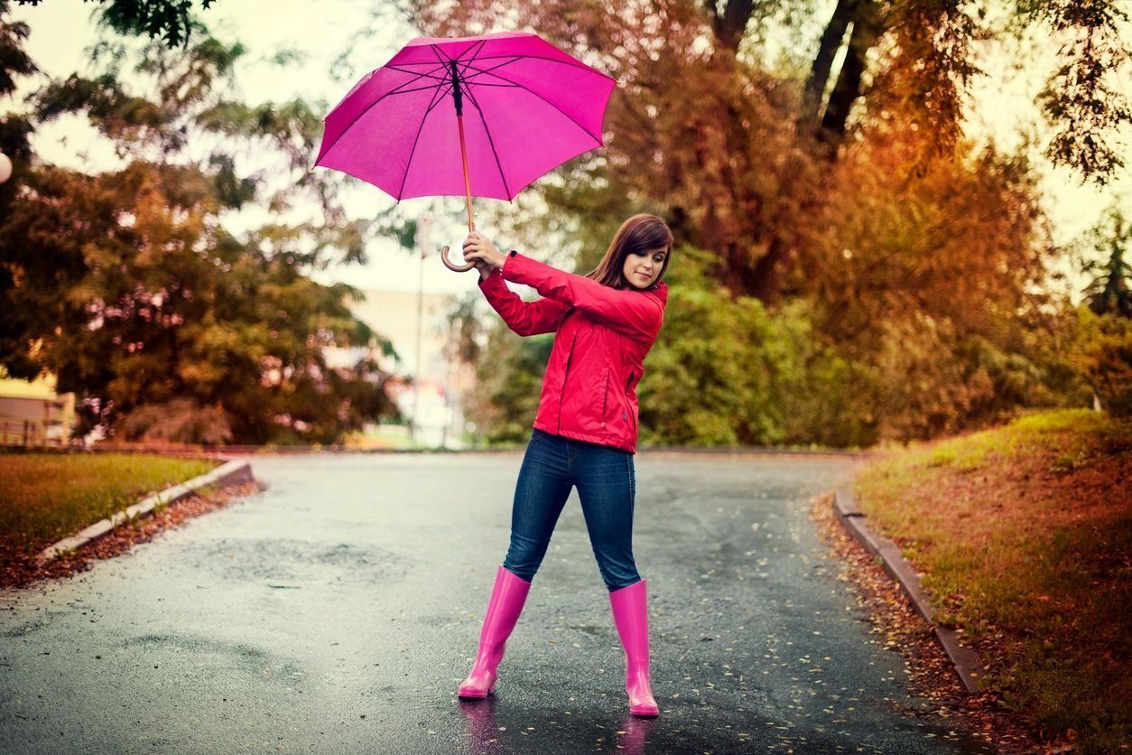 A woman in a red jacket and pink boots is holding a pink umbrella.