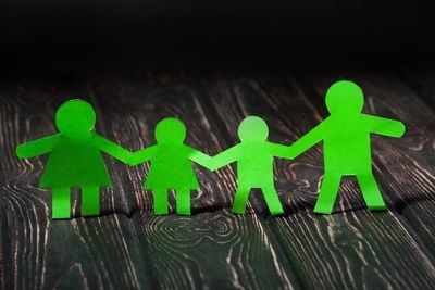 Green paper people cutouts A paper cut out of a family holding hands on a wooden table.