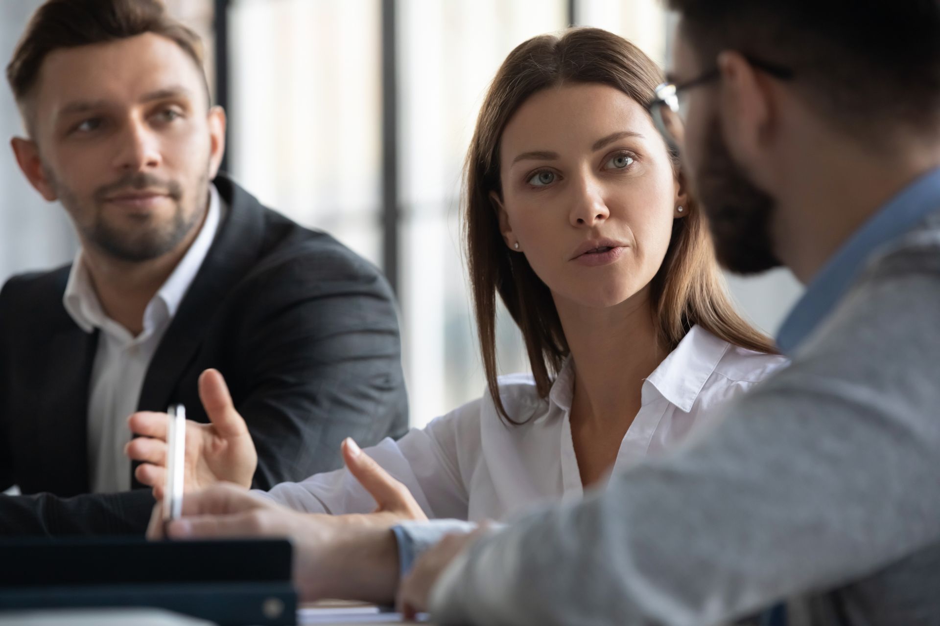 Three coworkers in a meeting, listening and discussing around a table. Three coworkers in a meeting, listening and discussing around a table.