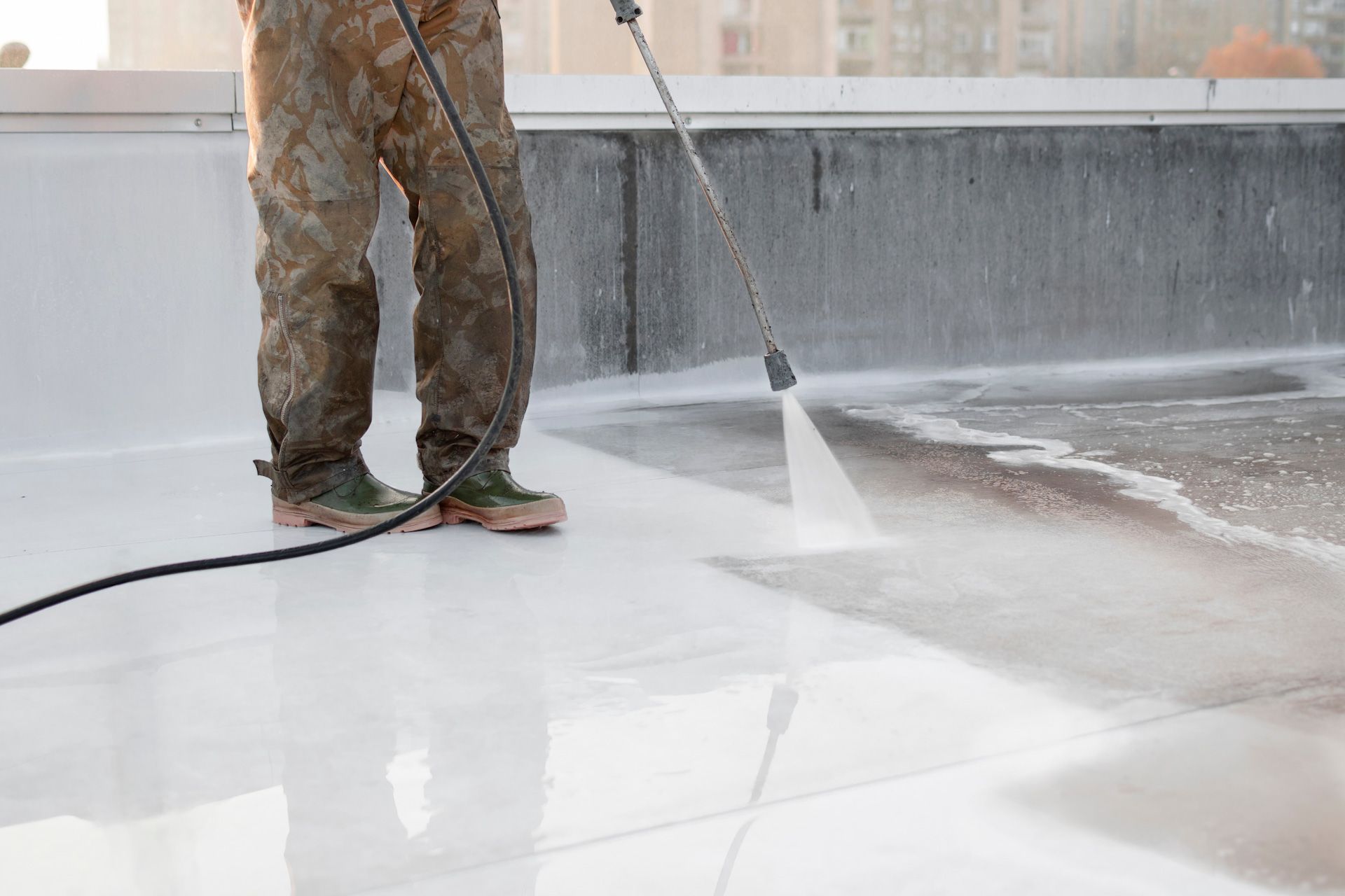 A man is using a high pressure washer to clean a roof.