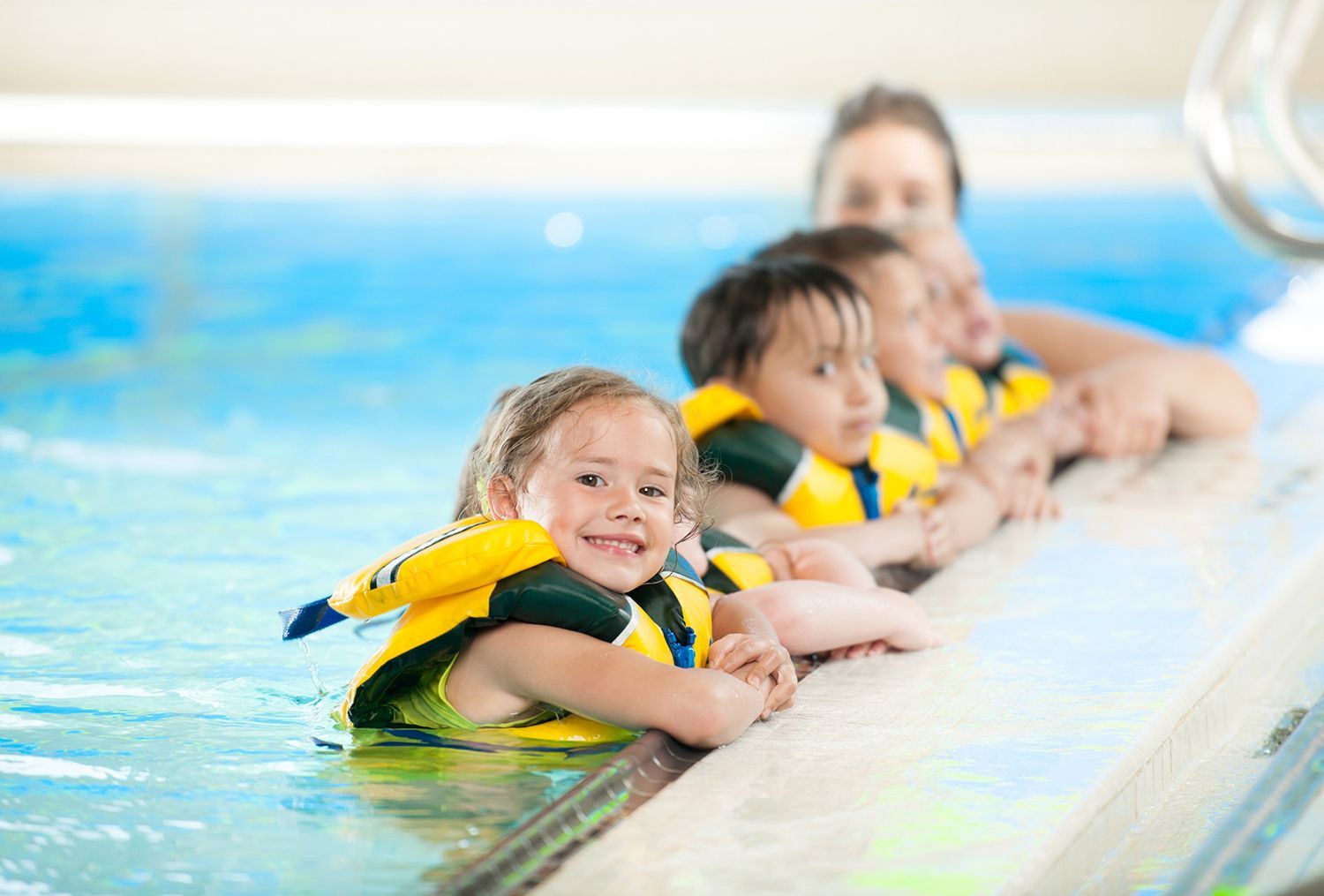 Children in yellow life jackets holding pool edge, smiling in a swimming pool