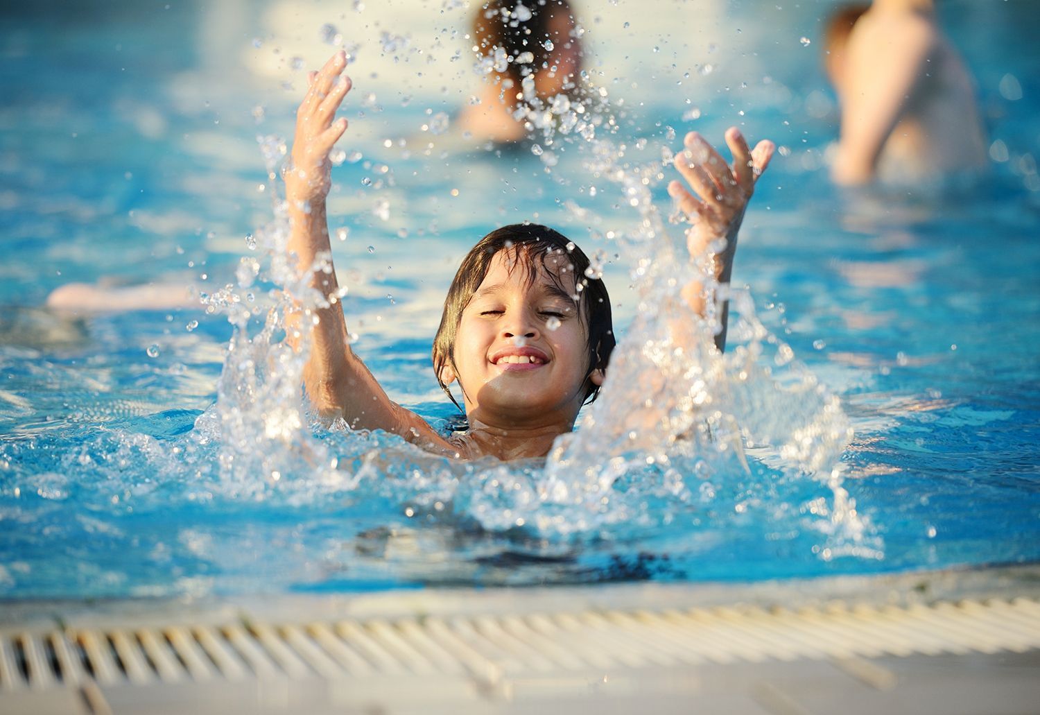Child splashing joyfully in a blue swimming pool with water spraying around them