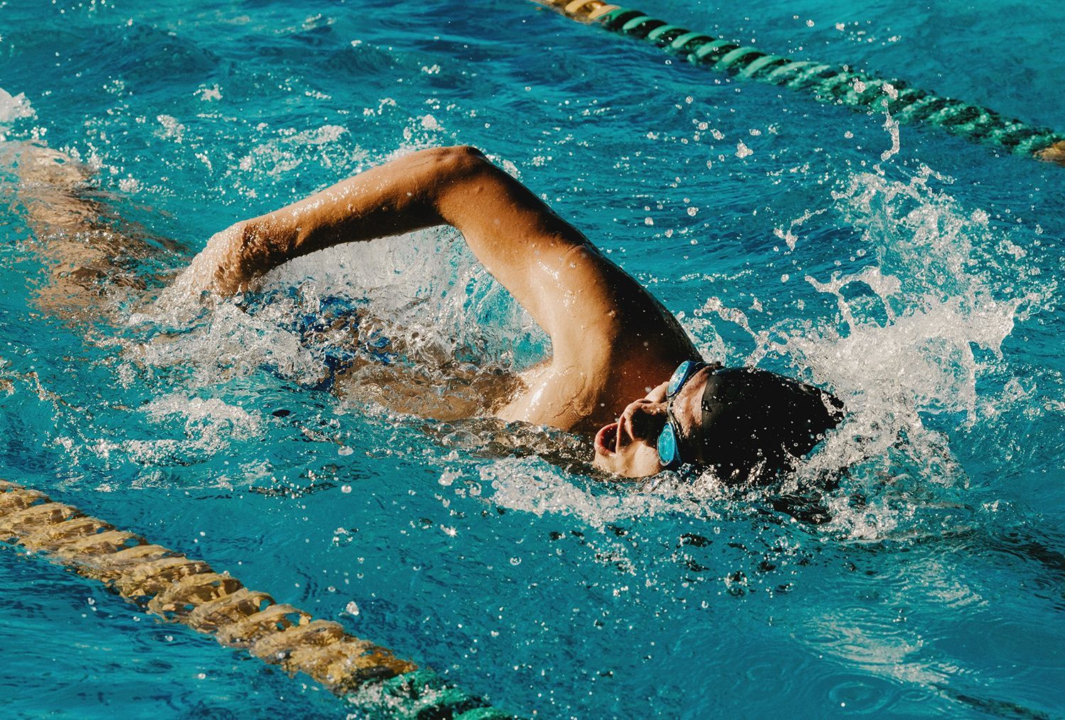 Swimmer doing freestyle in a blue pool, splashing water beside lane ropes
