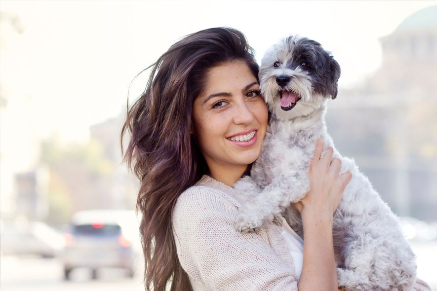 Woman holding a small black-and-white dog outdoors, both smiling in soft sunlight.