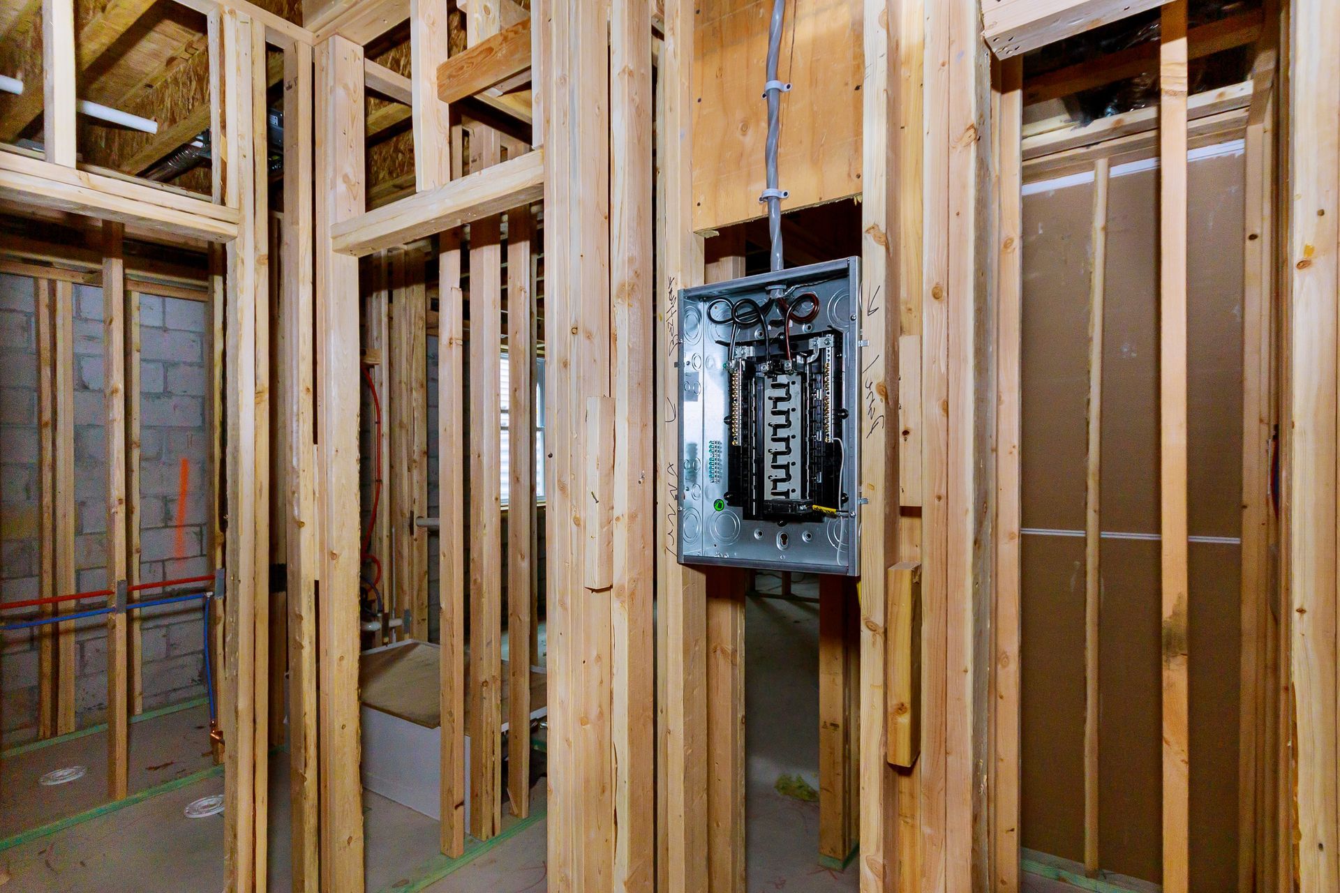 Framed interior wall with an electrical panel installed; studs are unfinished wood.