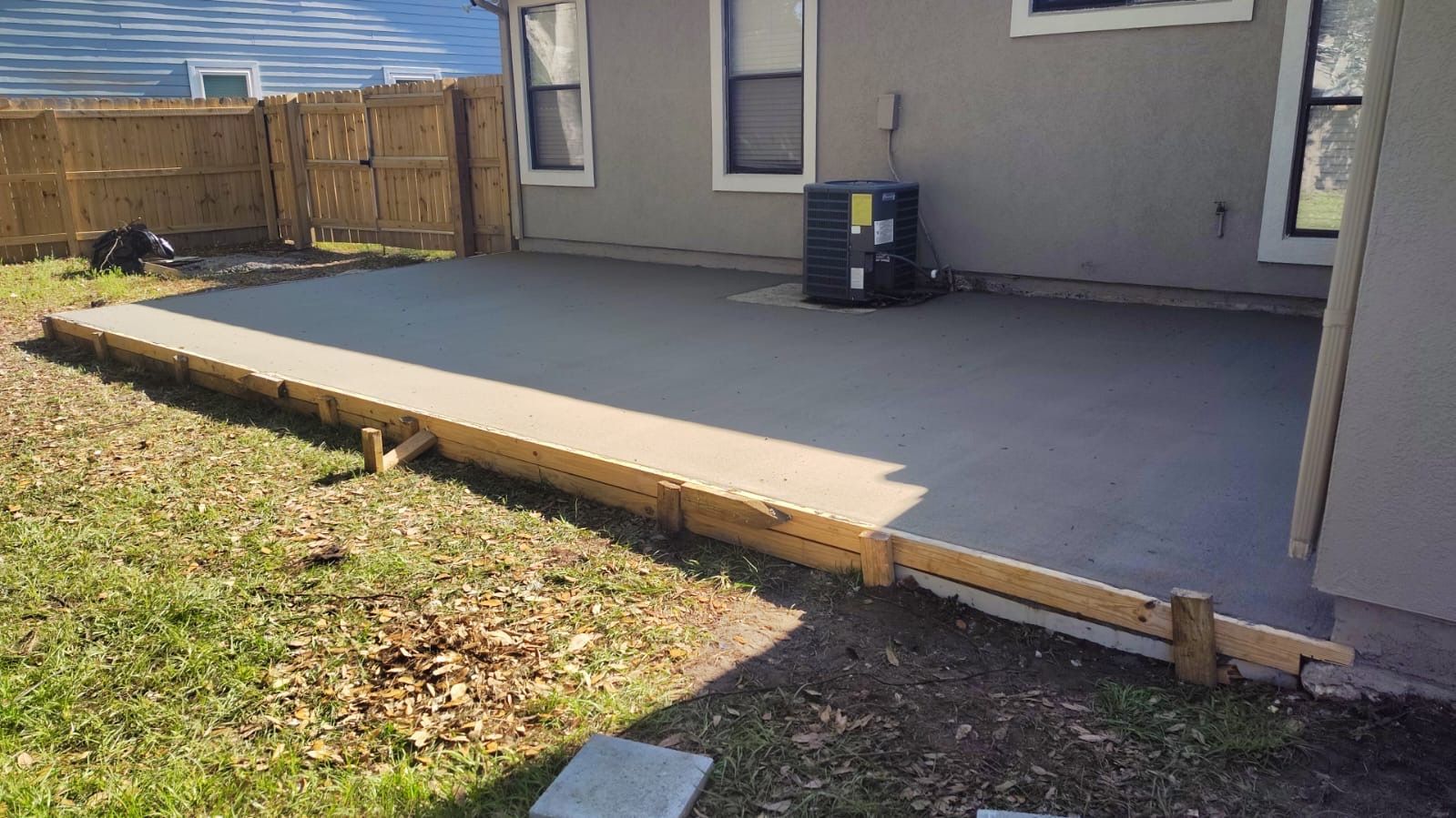 Concrete patio under construction next to a house with exposed brick and siding.