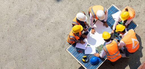 A group of construction workers are sitting around a table looking at a blueprint.