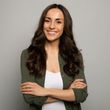 A woman with long hair is smiling with her arms crossed.