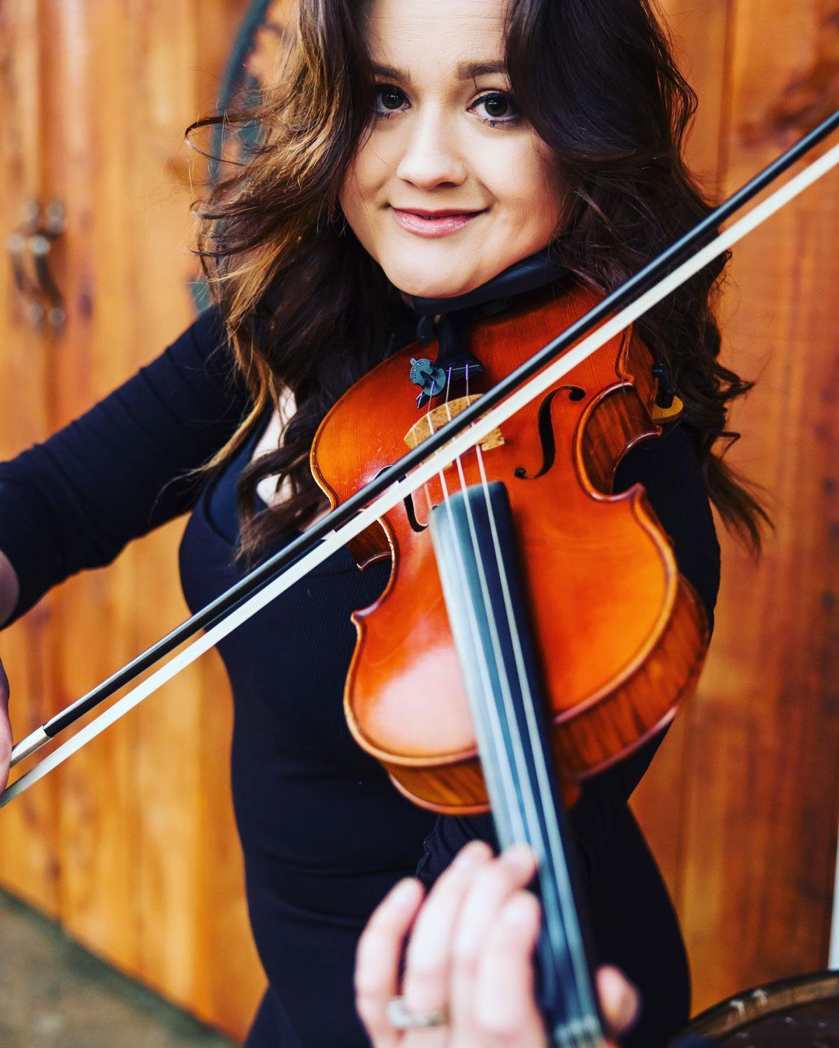 Smiling violinist playing a violin against a warm wooden background